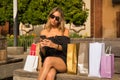 Young woman checking social networks on her cell phone sitting on a bench surrounded by shopping bags Royalty Free Stock Photo