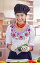 Young woman chef wearing traditional andean blouse, black cooking hat, vegetables on desk, shredding cucumber into deep