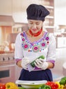 Young woman chef wearing traditional andean blouse, black cooking hat, vegetables on desk, shredding cucumber into deep