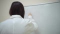 Girl in lab coat writes on board general formula for electrolysis of water.