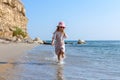 Child girl in summer dress with straw hat is running barefoot in shallow sea water