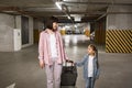 Young woman with child holding traveling suitcase as searching for car. Royalty Free Stock Photo