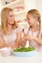 Young woman with child splitting pea in kitchen