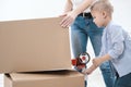 A young woman and a child stick cardboard boxes with a dispenser and adhesive tape. Royalty Free Stock Photo