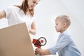 A young woman and a child stick cardboard boxes with a dispenser and adhesive tape. Royalty Free Stock Photo