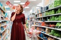 A young woman chooses products, holding a grocery cart with a baby sitting in it. Indoor. The concept of shopping and consumerism Royalty Free Stock Photo