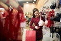 Young woman chooses brassiere among set in a boutique. Pretty girl considers bra with shopping bags in her hand in Royalty Free Stock Photo