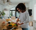 Young woman chopping vegetables in kitchen at home, happy and smiling Royalty Free Stock Photo