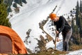 Young woman chopping wood with an ax near a tourist tent in the mountains against a background of snow-covered forest on a sunny d Royalty Free Stock Photo