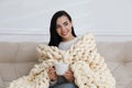 Young woman with chunky knit blanket and cup on sofa at home Royalty Free Stock Photo