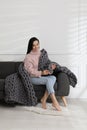 Young woman with chunky knit blanket on sofa at home Royalty Free Stock Photo