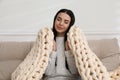 Young woman with chunky knit blanket on sofa at home Royalty Free Stock Photo