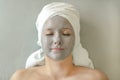 Young woman with clay mask on face and towel on head in form of turban lies with closed eyes and enjoys spa treatment Royalty Free Stock Photo