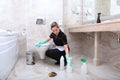 A young woman in a cleaning service uniform cleans the toilet in the bathroom. Marble floor tiles. The concept of cleanliness and