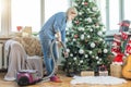 Young woman cleaning with vacuum cleaner, vacuuming under Christmas Tree needles with New Years ornaments on hardwood Royalty Free Stock Photo