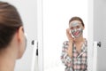 Young woman with cleansing mask on her face near mirror in bathroom Royalty Free Stock Photo