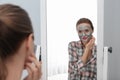 Young woman with cleansing mask on her face near mirror. Skin care Royalty Free Stock Photo