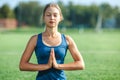 Young woman with closed eyes in a blue shirt enjoying meditation and yoga on green grass in the summer on nature. Royalty Free Stock Photo