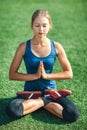 Young woman with closed eyes in a blue shirt and leggings enjoying meditation and yoga on green grass in the summer on nature. Royalty Free Stock Photo