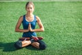 Young woman with closed eyes in a blue shirt and leggings enjoying meditation and yoga on green grass in the summer on nature. Royalty Free Stock Photo