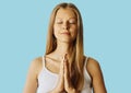 Young woman with closed eyes and hands in praying gesture. Meditation, balance and peace of mind concept.  over blue Royalty Free Stock Photo