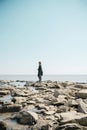 Young woman in a coat and scarft with camera standing on a deserted beach in cold weather Royalty Free Stock Photo