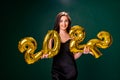 Young woman in cocktail dress with bright make-up celebrating New Year 2022 and holding golden balloons 2022 in hands on Royalty Free Stock Photo