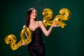 Young woman in cocktail dress with bright make-up celebrating New Year 2022 and holding golden balloons 2022 in hands on Royalty Free Stock Photo