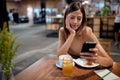 Young woman at coffee shop having breakfast and looking at her phone Royalty Free Stock Photo