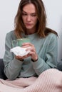 Young woman with a cold sits with a napkin and a mug, looking sickly