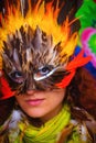 Young woman with a colorful feather carnival face mask on bright colorful background, eye contact, make up artist. Royalty Free Stock Photo