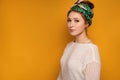 Young woman with a kerchief looks at the camera over yellow background