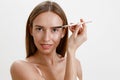 Pretty young woman with healthy skin combing her eyebrows with brush over white studio background Royalty Free Stock Photo