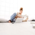 Young woman with computer reading a book, sitting on the floor i Royalty Free Stock Photo