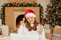 Young woman congratulating with Christmas her close people while sitting on floor in front of tree with her laptop, having happy Royalty Free Stock Photo