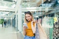 Young woman consumer in the mall browses chat and uses using a smartphone. female standing with a mobile phone in her hands in Royalty Free Stock Photo