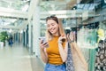 Young woman consumer in the mall browses chat and uses using a smartphone. female standing with a mobile phone in her hands in Royalty Free Stock Photo