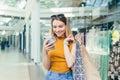 Young woman consumer in the mall browses chat and uses using a smartphone. female standing with a mobile phone in her hands in Royalty Free Stock Photo