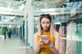 Young woman consumer in the mall browses chat and uses using a smartphone. female standing with a mobile phone in her hands in Royalty Free Stock Photo