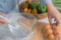 Young woman cooking in a bright kitchen, hand made cracked fresh egg yolks dripping into the bowl. Preparing ingredients for