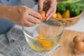 Young woman cooking in a bright kitchen, hand made cracked fresh egg yolks dripping into the bowl. Preparing ingredients for