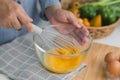 Young woman cooking in bright kitchen, hands whisking eggs in a bowl placed on towel and wooden table. Preparing ingredients for Royalty Free Stock Photo