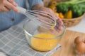 Young woman cooking in bright kitchen, hands whisking eggs in a bowl placed on towel and wooden table. Preparing ingredients for Royalty Free Stock Photo