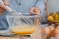 Young woman cooking in bright kitchen, hands whisking eggs in a bowl placed on towel and wooden table. Preparing ingredients for Royalty Free Stock Photo