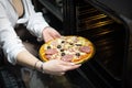 Young woman cooking pizza in kitchen. Raw pizza in the hands of a housewife. Sexy woman puts pizza in a hot oven Royalty Free Stock Photo