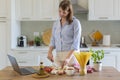 A young woman cooks at home in the kitchen, she watches a video recipe on a laptop and works with the dough on the table, she cuts Royalty Free Stock Photo