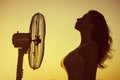 Young Woman cooling herself during hot weather in front of fan on a blue sunset sky background Royalty Free Stock Photo