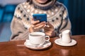 Young woman copywriter or blogger works with social networks on her smartphone while sitting in a coffee shop and sipping hot