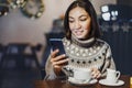 Young woman copywriter or blogger works with social networks on her smartphone while sitting in a coffee shop and sipping hot