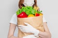 Young woman courier volunteer wearing a medical mask holds a paper bag with products vegetables chili herbs over white